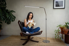 Load image into Gallery viewer, Woman crocheting in an arm chair, using a floor lamp.