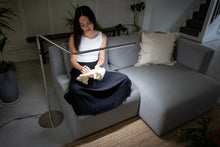 Load image into Gallery viewer, Woman crocheting on a sofa in dim light but with a floor lamp illuminating the work.
