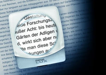 Load image into Gallery viewer, Ultra flat, circular magnifying lens with square, clear casing. Displayed on page, magnifying text.