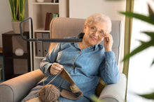 Load image into Gallery viewer, Woman sitting in an arm chair using the Electra lamp to knit.