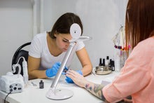 Load image into Gallery viewer, Nail technician working on a client's nails with a Halo Go magnifying lamp in a salon setting.
