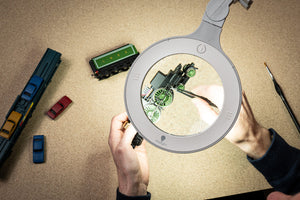Image of magnifying lamp being used to paint a green miniature train.