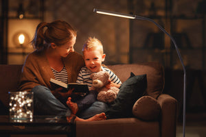 Mother and young boy with a teddy bear, reading a book, sitting on a couch with the Electra lamp next to the couch.