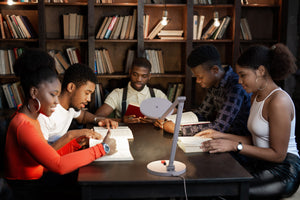 Young group of people studying in library with Daylight's Tricolour lamp on table.